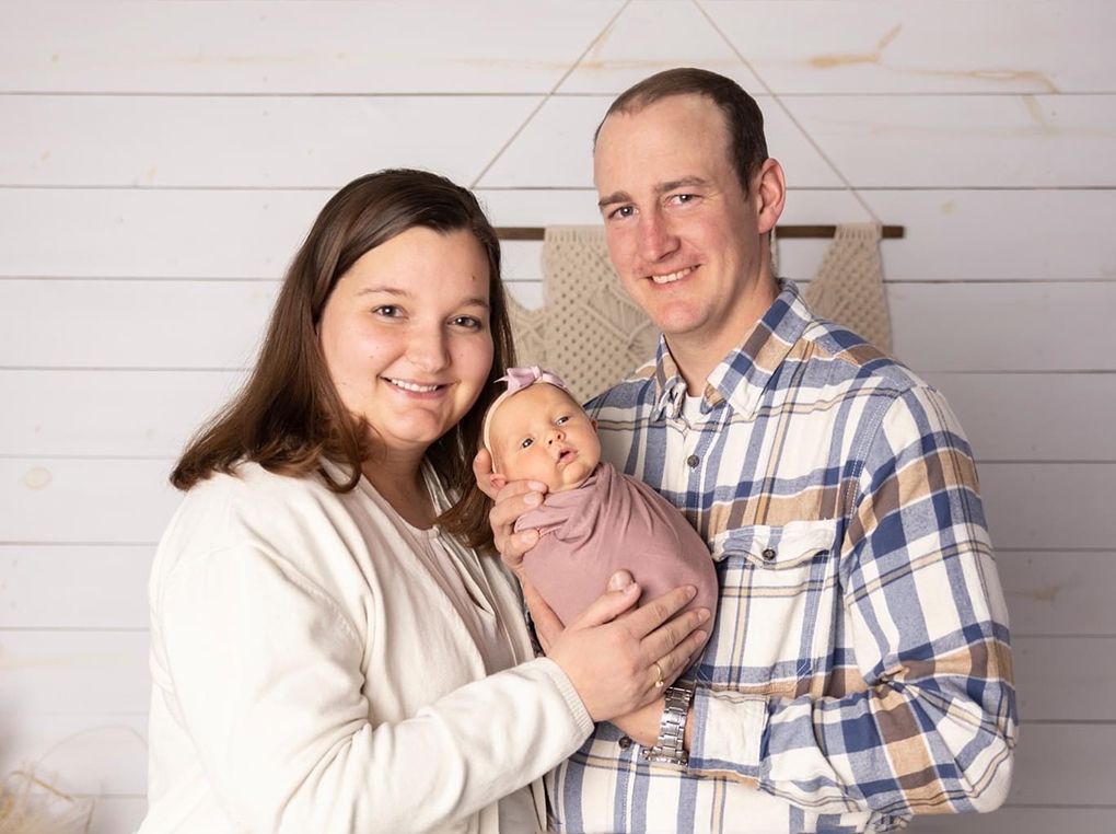 Elizabeth and Darren Radil smile with their newborn baby girl Esther in a photo studio