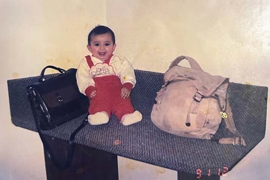 Baby Lezan Tahir sits next to his parents’ luggage while they were fleeing persecution in the Middle East during the Gulf War