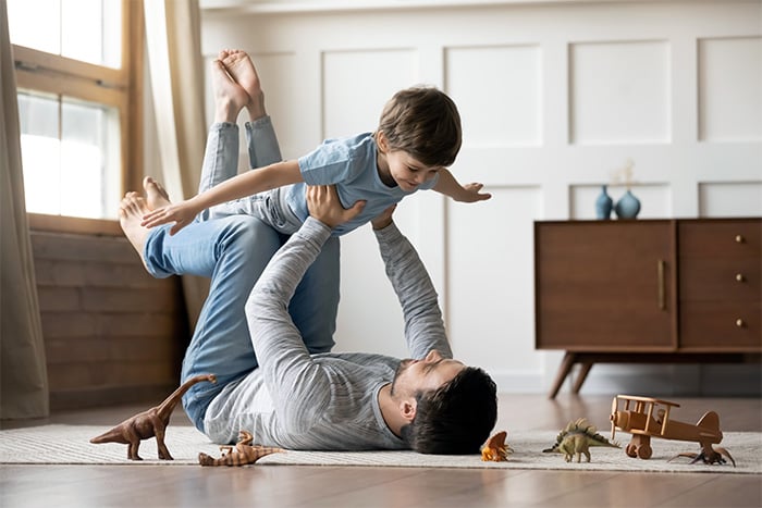 happy father lays back and lifts son into air after securing great health and life insurance
