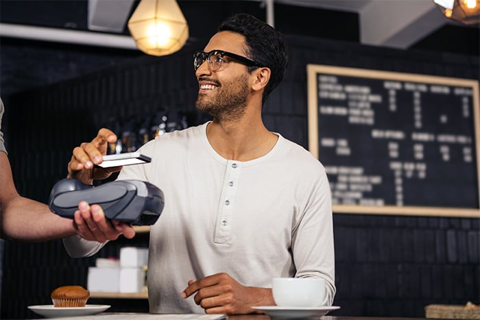 man with white shirt and glasses smiles as he buys a muffin using his mobile wallet