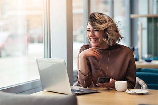 happy woman enjoys easy online credit card access while sitting at table with coffee phone and computer