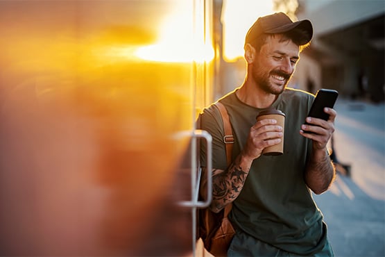 Relaxed young man with a cup of coffee, checking his Gate City Bank app while enjoying a beautiful sunrise in Bismarck, ND