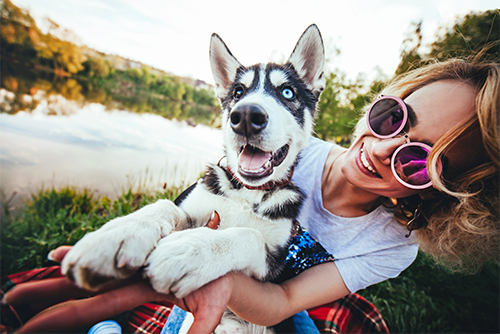 Smiling woman holding a husky outside her lake home in MN, purchased with a Gate City Bank MinnStart home loan