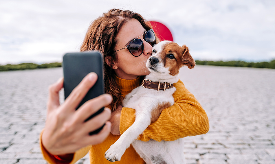 Curly-haired young woman kissing her terrier and taking a selfie outside her nearest Gate City Bank
