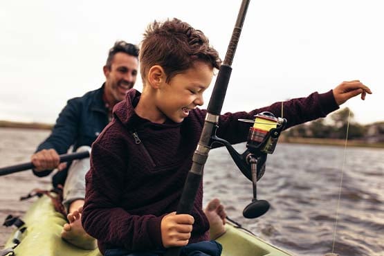 Young boy in a kayak with his dad, reeling in a fish out on Devils Lake