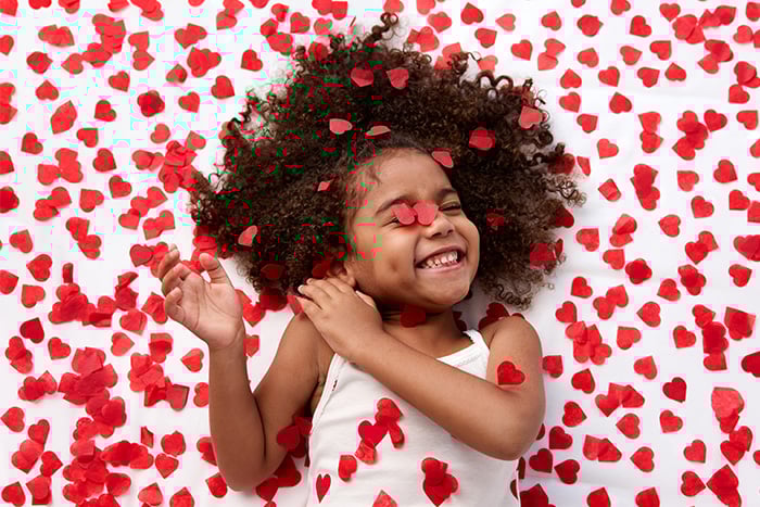 A young girl giggles while surrounded by red confetti hearts.