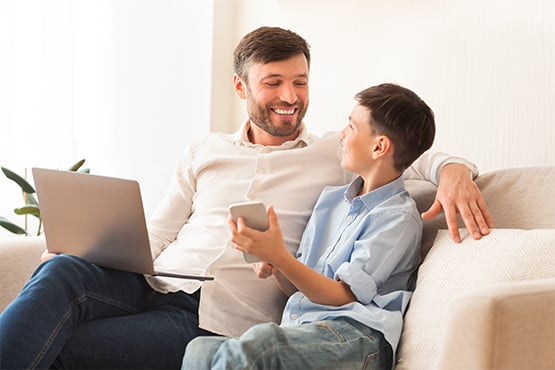happy father and son sit on couch with phone and plan for financial future