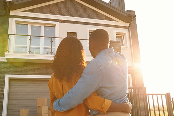 couple stands in yard and looks up at house with bright sunlight
