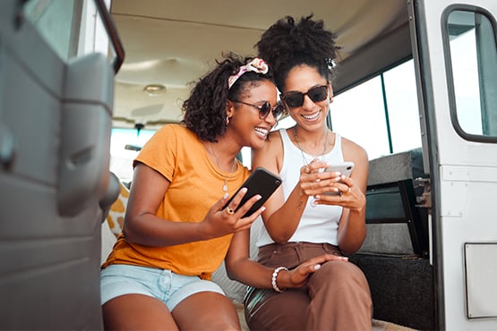two female friends in sunglasses sit together in a van and sunshine while practicing phone security best practices from Gate City Bank