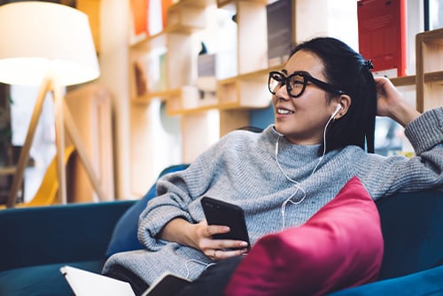 Relaxed Gen Z woman with earbuds and black rimmed glasses, applying for a debt consolidation loan on her phone in Fargo, ND