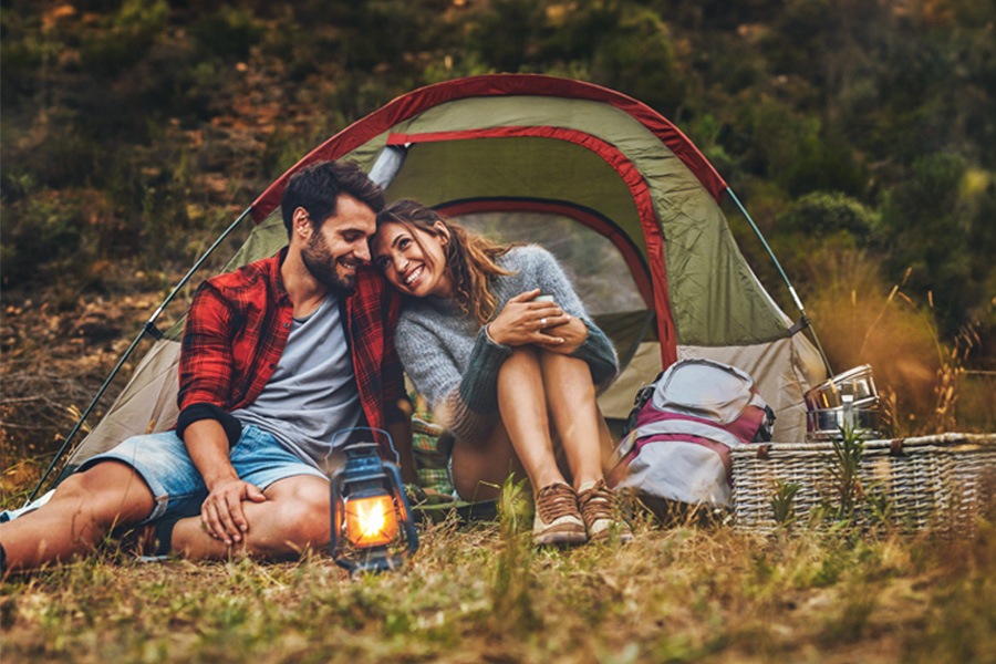 Smiling couple, sitting side-by-side and camping with a tent outside of Elk River, Minnesota