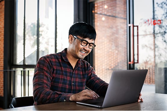 happy man with glasses sits and checks online statements and notices with laptop
