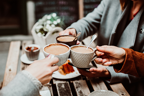 Three friends saying cheers with cups of hot cocoa, after meeting up in a café in Elk River, MN 