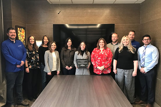 Gate City Bank mortgage team members gather around their recently earned affordable housing award in a conference room