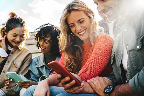 Group of young friends sitting on bleachers in sunny Fargo, ND, opening new Gate City Bank checking accounts via mobile