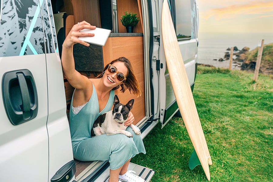 Woman in sunglasses taking a selfie with her Boston terrier, sitting in her camper van purchased with a Gate City Bank loan