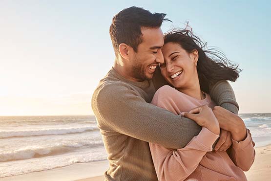 Laughing couple hugging on a windy beach after redeeming Gate City Bank debit card reward points for free airfare