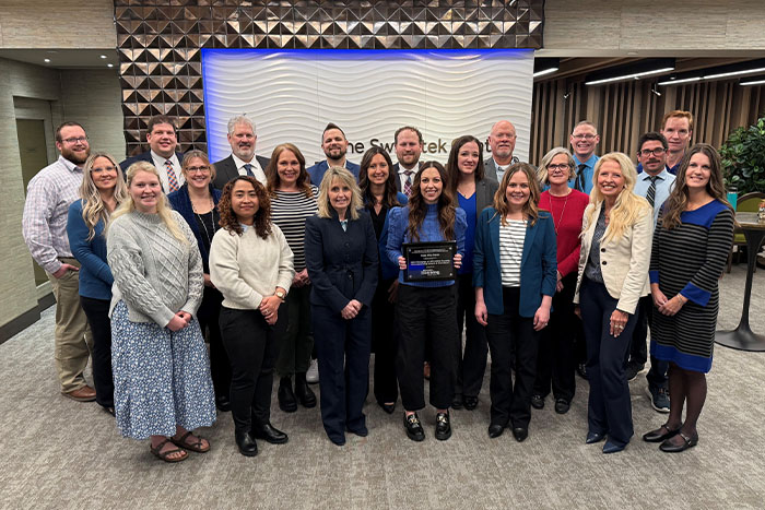 A large group of Gate City Bank mortgage team members huddle around the NDHFA Affordable housing Award for 2023
