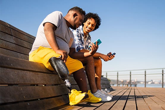 two happy male friends sit together and use phone to move money