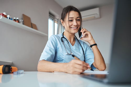 smiling doctor in light blue scrubs, talking on the phone in her office with her Fargo mortgage loan lender at Gate City Bank
