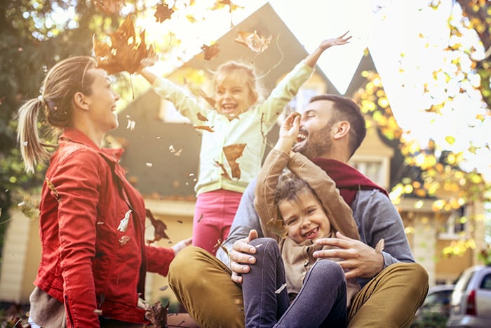 happy young family plays in leaves outside after securing liability umbrella insurance