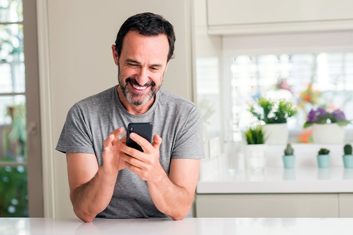 happy man in light gray t-shirt holds his smartphone and avoids scammers while banking