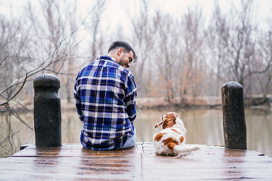 Young man in flannel with his King Charles spaniel, sitting on a dock near Sauk Rapids, Minnesota