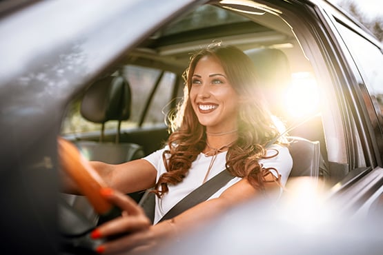 Smiling woman drives her car with sunset in the background after learning helpful auto buying tips from Gate City Bank