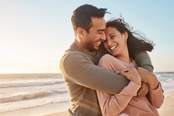 Laughing couple hugging on a windy beach after redeeming Gate City Bank debit card reward points for free airfare