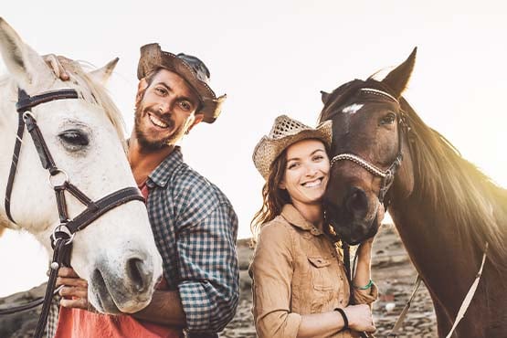 Smiling rancher couple holding the reins of two relaxed horses at sunset on the outskirts of Minot, ND