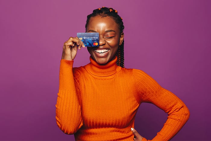 Young woman in orange turtleneck, holding up her Gate City Bank debit card after opening a new checking account in St. Cloud, MN