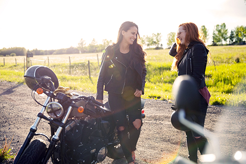 two girls laughing on a ND country road beside their motorcycles purchased with Gate City Bank loans