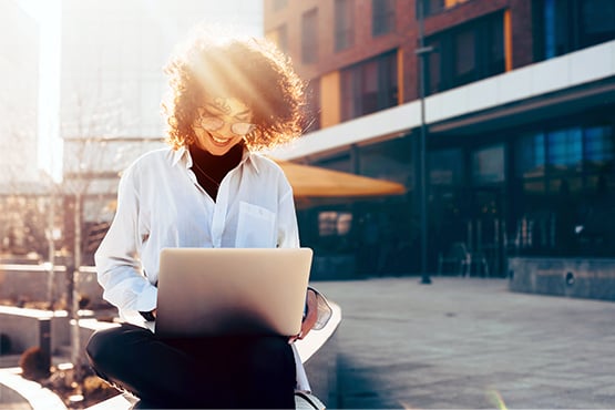 smiling woman uses laptop on a sunny day outdoors to keep fraud attempts at bay with gate city bank