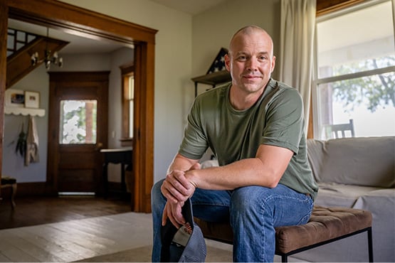 : a service member sits and smiles at the camera at home after learning about financial military benefits from Gate City Bank