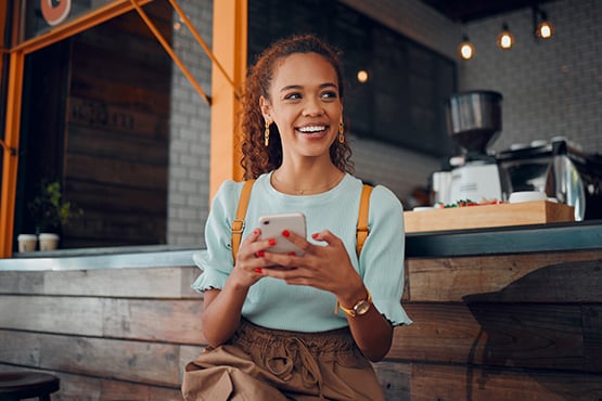 Smiling teen in a light aqua t-shirt opening a Totally Free Checking account on her smartphone at a Fargo coffee shop
