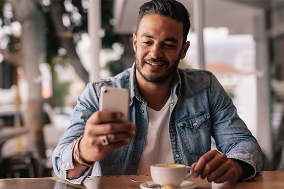 happy man in coffee shop uses phone for Gate City Bank’s payment methods