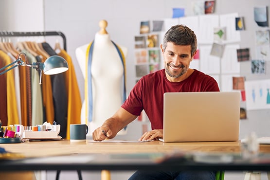 man in a red t-shirt uses laptop to research how to get a business loan