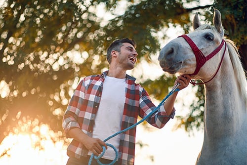Man in plaid shirt and white horse walking together on a hobby farm, purchased with a Gate City Bank home loan in rural ND