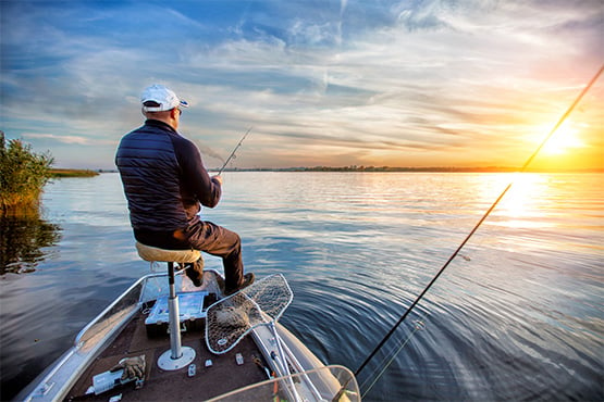 relaxed gentleman in a baseball cap fishing at sunset after getting a boat loan from Gate City Bank
