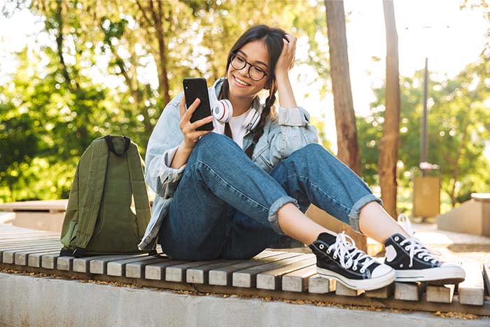 Smiling brunette with long braids, reading the easy steps to consolidate her student loans with Gate City Bank on her phone