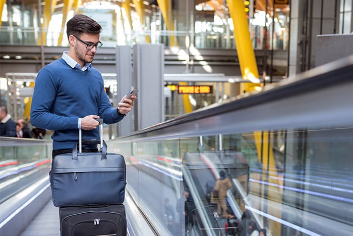 happy man in blue sweater stands next to train and uses bill pay on smartphone