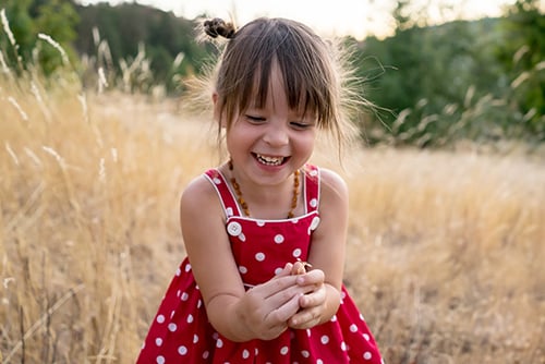 Happy little girl with pigtails in a red polka dot dress, playing in a sunny wheat field in rural North Dakota