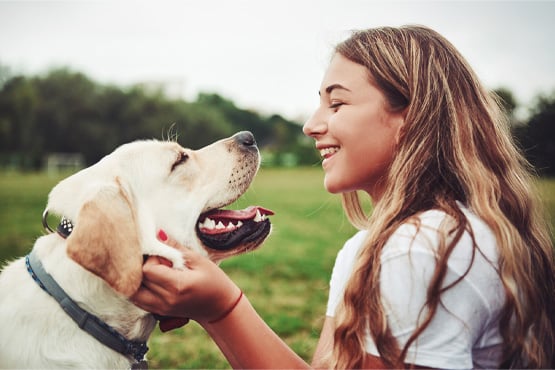 Teen girl with wavy hair, a local Gate City Bank checking customer in Fargo, ND, smiling at her golden Labrador retriever