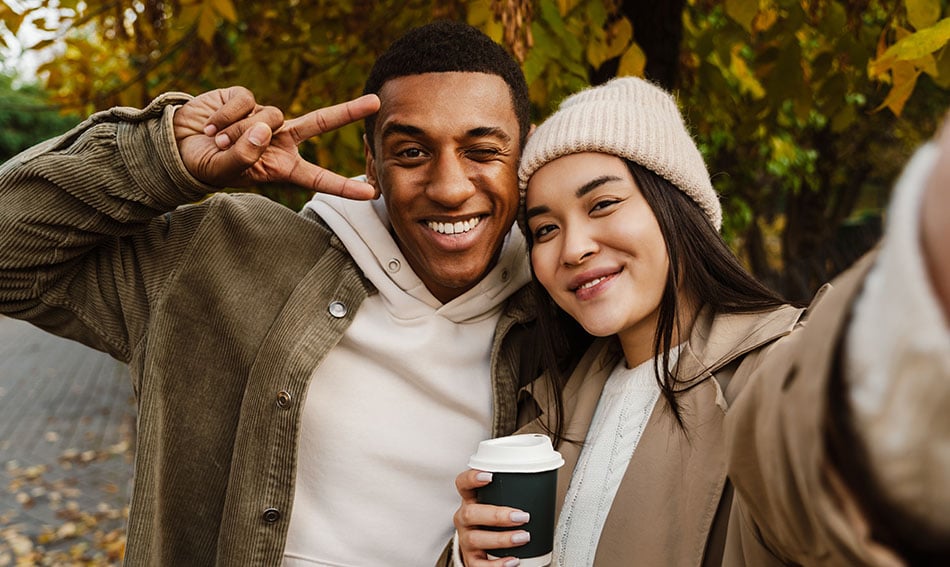 Two friends in fall jackets, taking a selfie at Island Park in Fargo after opening their checking accounts