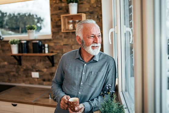 Senior gentleman drinking coffee while looking out his window on a winter day in Bismarck, ND