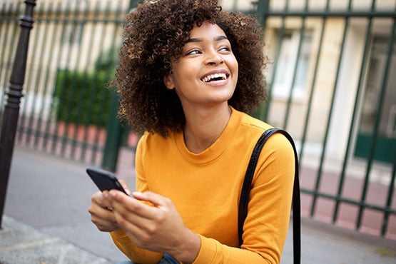 Cheerful young woman sitting on step with her phone after opening her new Gate City Bank checking account