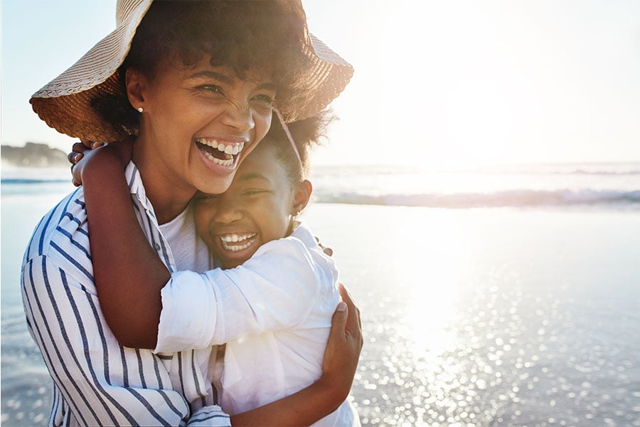 Mom and daughter hugging and laughing together on beach after earning free airfare with Gate City Bank’s debit card rewards