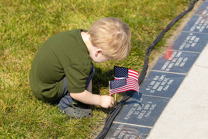 boy plants American flag next to marker at Veterans Memorial Park in Grand Forks ND