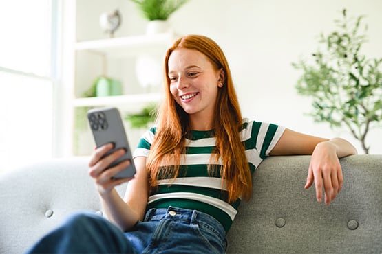 Gen Z redhead smiling while using AI for financial advice on her smartphone at her apartment in Fargo, ND