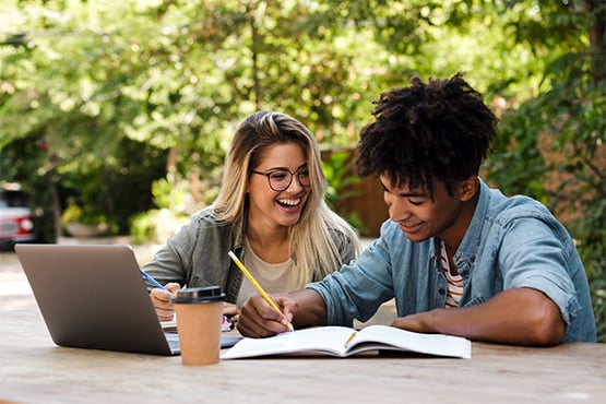 Two teenage students smiling and working on homework together